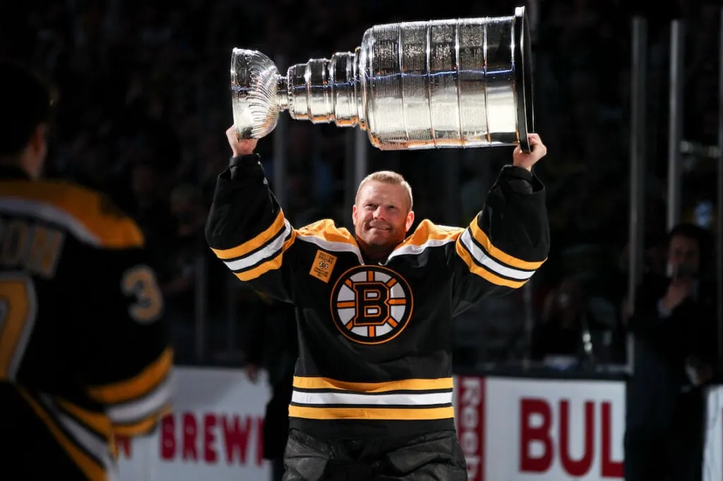 Tim Thomas in his Boston Bruins hockey jersey holding up the Stanley Cup trophy after the Bruins won in 2011.
